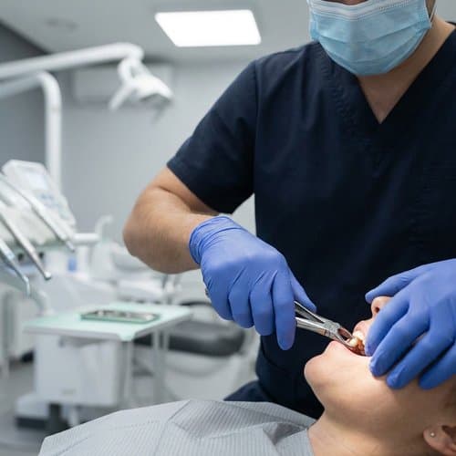 Dentist performing a tooth extraction with forceps while the patient rests in the dental chair