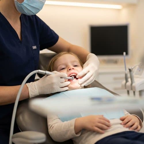 Dentist providing gentle preventive care to a child in the dental chair